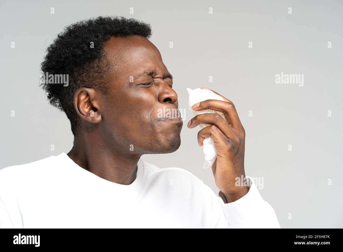 L'homme noir soufflant le nez et éternuant dans les tissus ou la serviette, a l'allergie, les premiers symptômes du rhume et de la grippe Banque D'Images