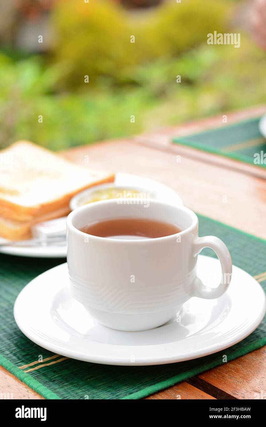 Thé chaud dans une tasse blanche avec pain grillé sur la table comme petit déjeuner Banque D'Images