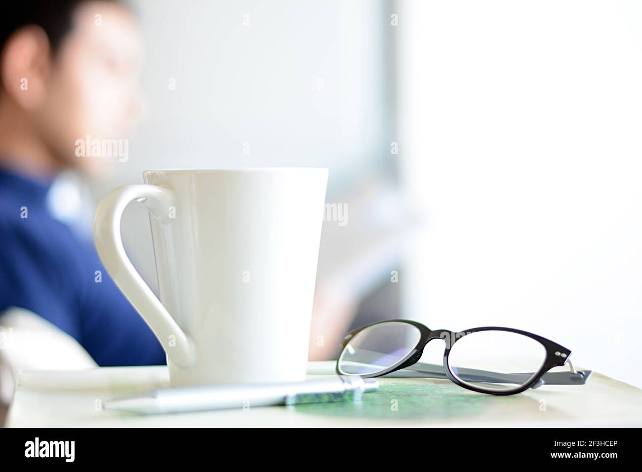 Tasse à café, lunettes et stylo sur un livre avec fond flou d'un livre de lecture d'homme Banque D'Images