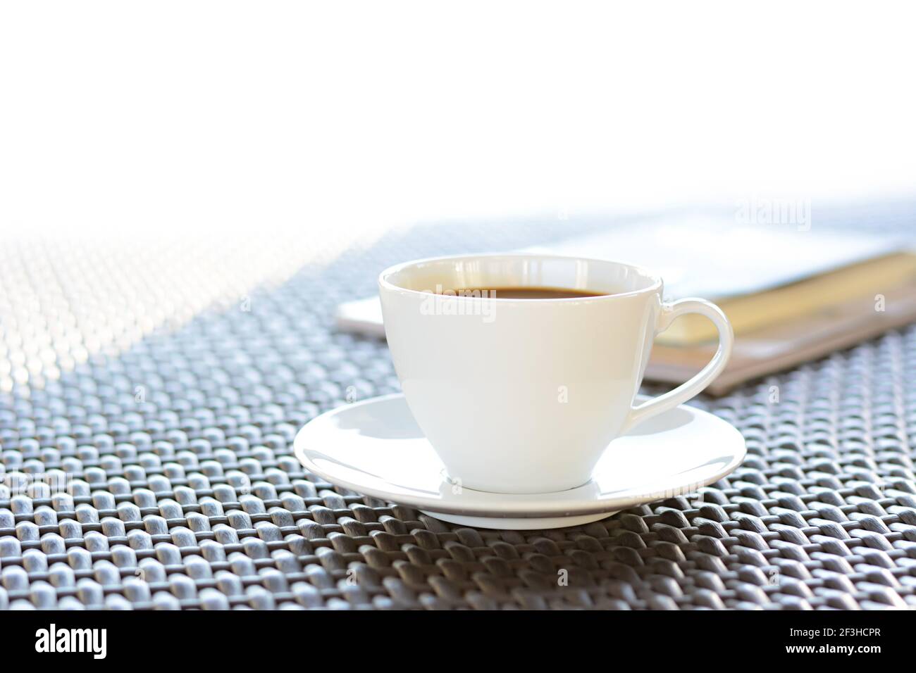 Tasse à café avec livre sur table en osier brun Banque D'Images