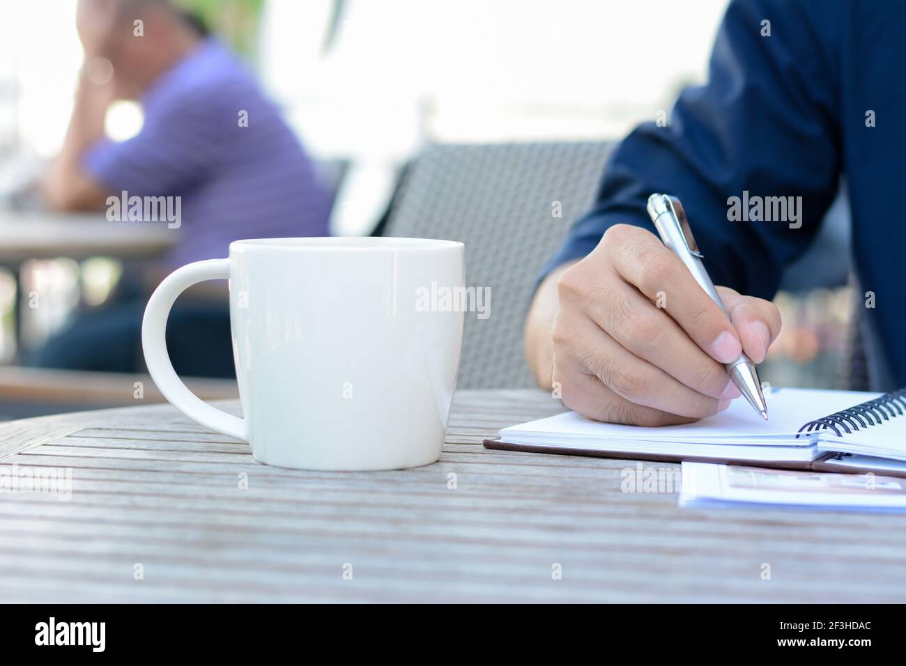 Un homme écrit à la main sur un carnet avec une tasse de café à côté Banque D'Images