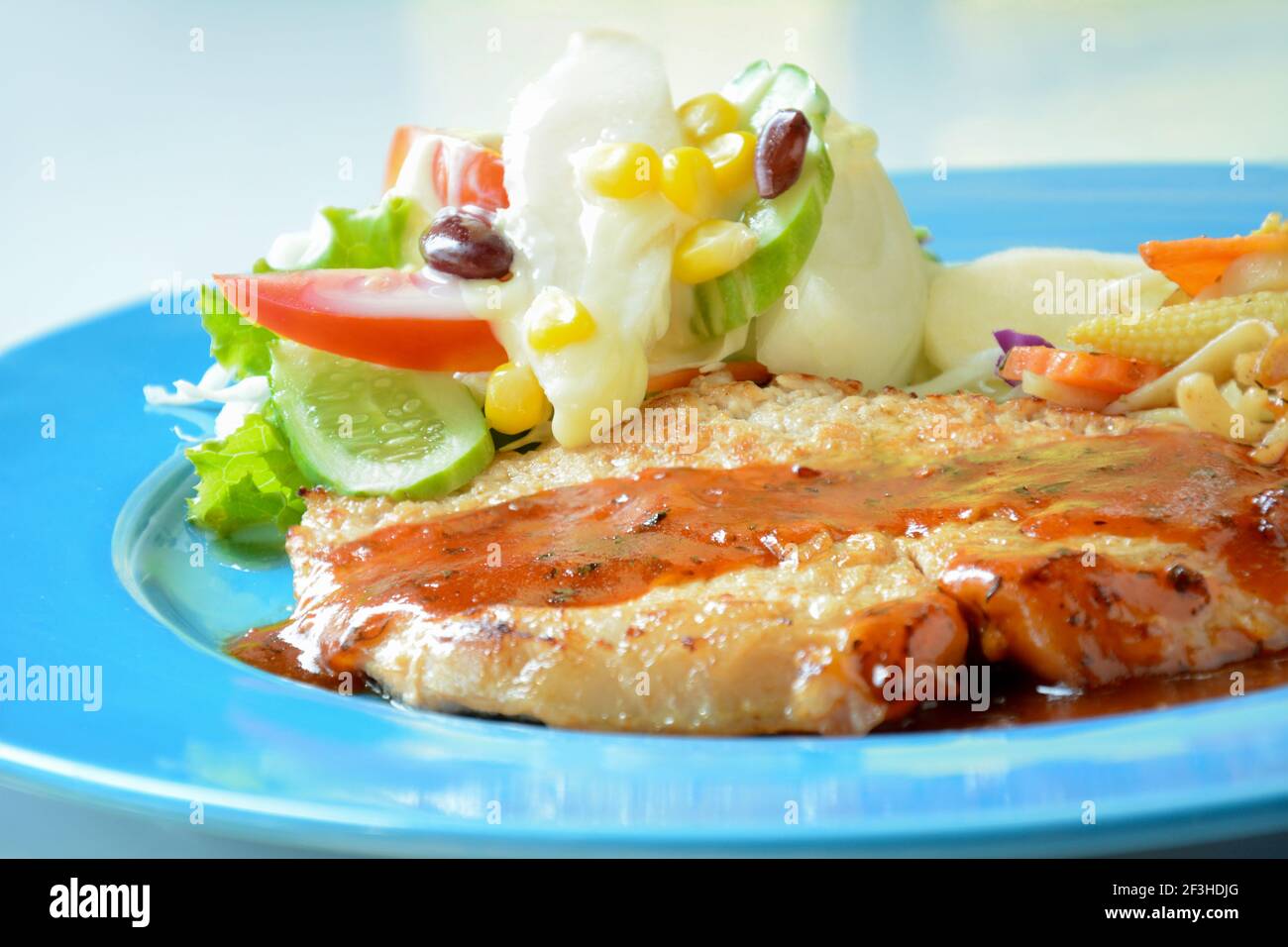 Rôti de porc poêlé avec salade de légumes sur coloré assiette bleue Banque D'Images