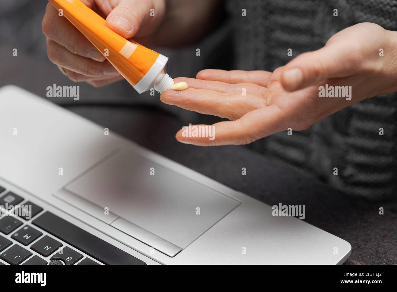 Mains de sexe féminin ou masculin appliquant de la crème pour les mains sur les doigts hydratez la peau tout en travaillant au bureau à domicile près de ordinateur portable Banque D'Images