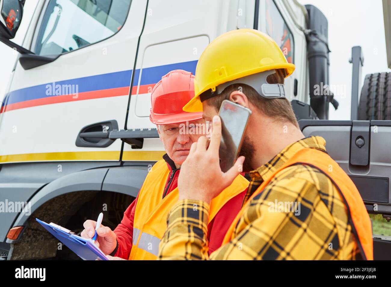 Le téléphone cellulaire du travailleur de la construction et la liste de contrôle vérifient la livraison du camion construction de routes Banque D'Images