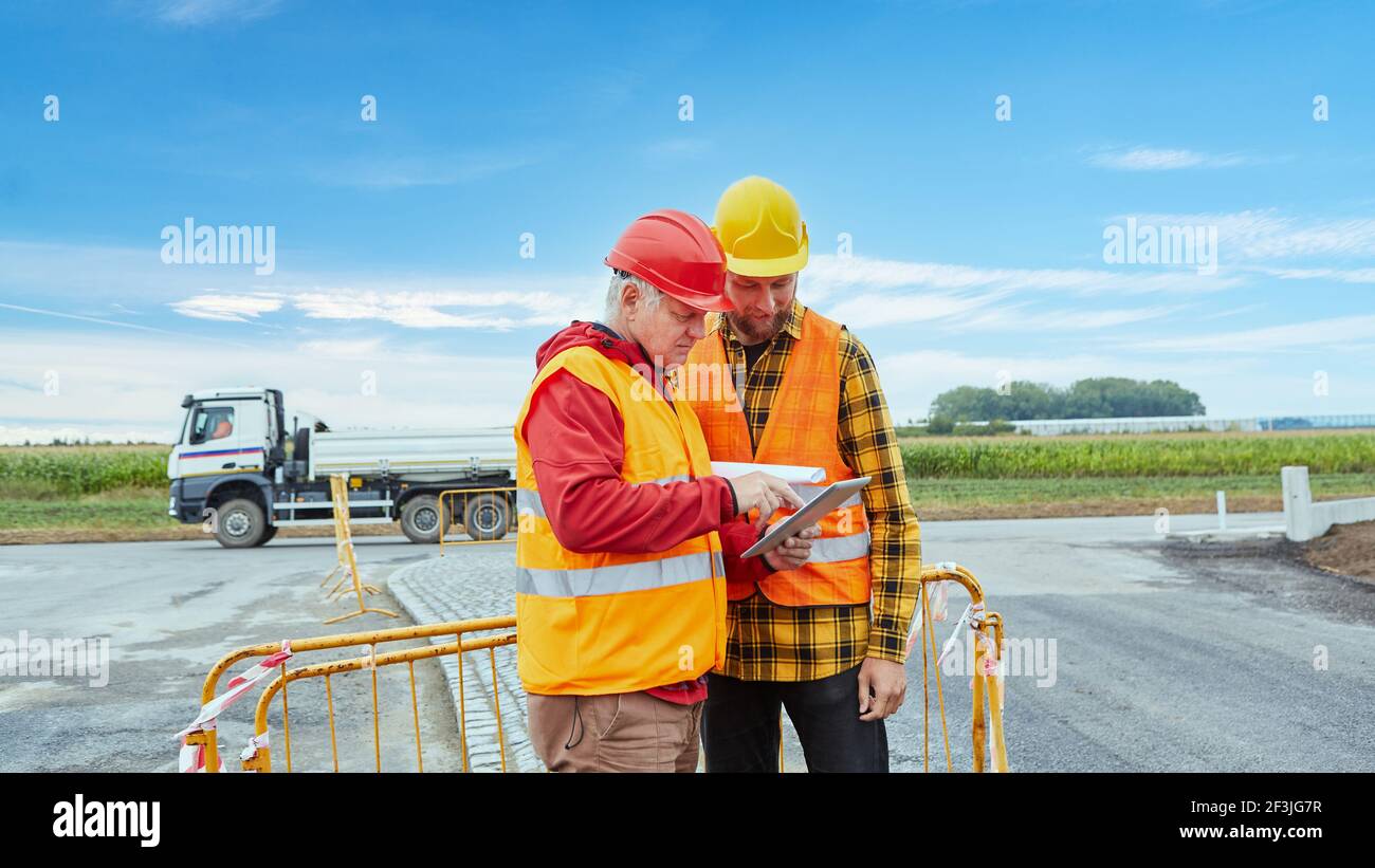 Deux ouvriers de la construction sur le chantier de planification avec un ordinateur tablette en ligne sur internet Banque D'Images