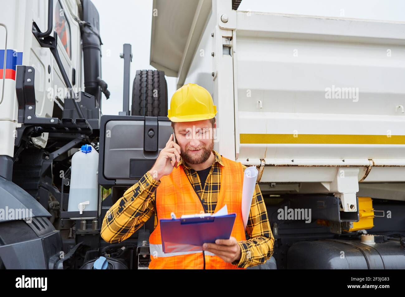 Travailleur de la construction ou chef de chantier avec liste de contrôle et smartphone dans avant du camion sur le chantier Banque D'Images