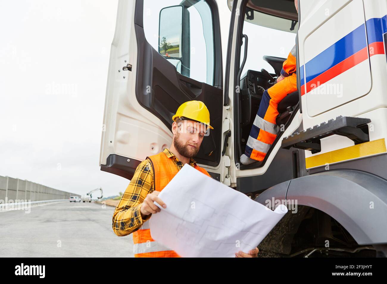 Le travailleur de la construction de routes se tient debout avec une carte sur le camion avec livraison de matériaux de construction Banque D'Images