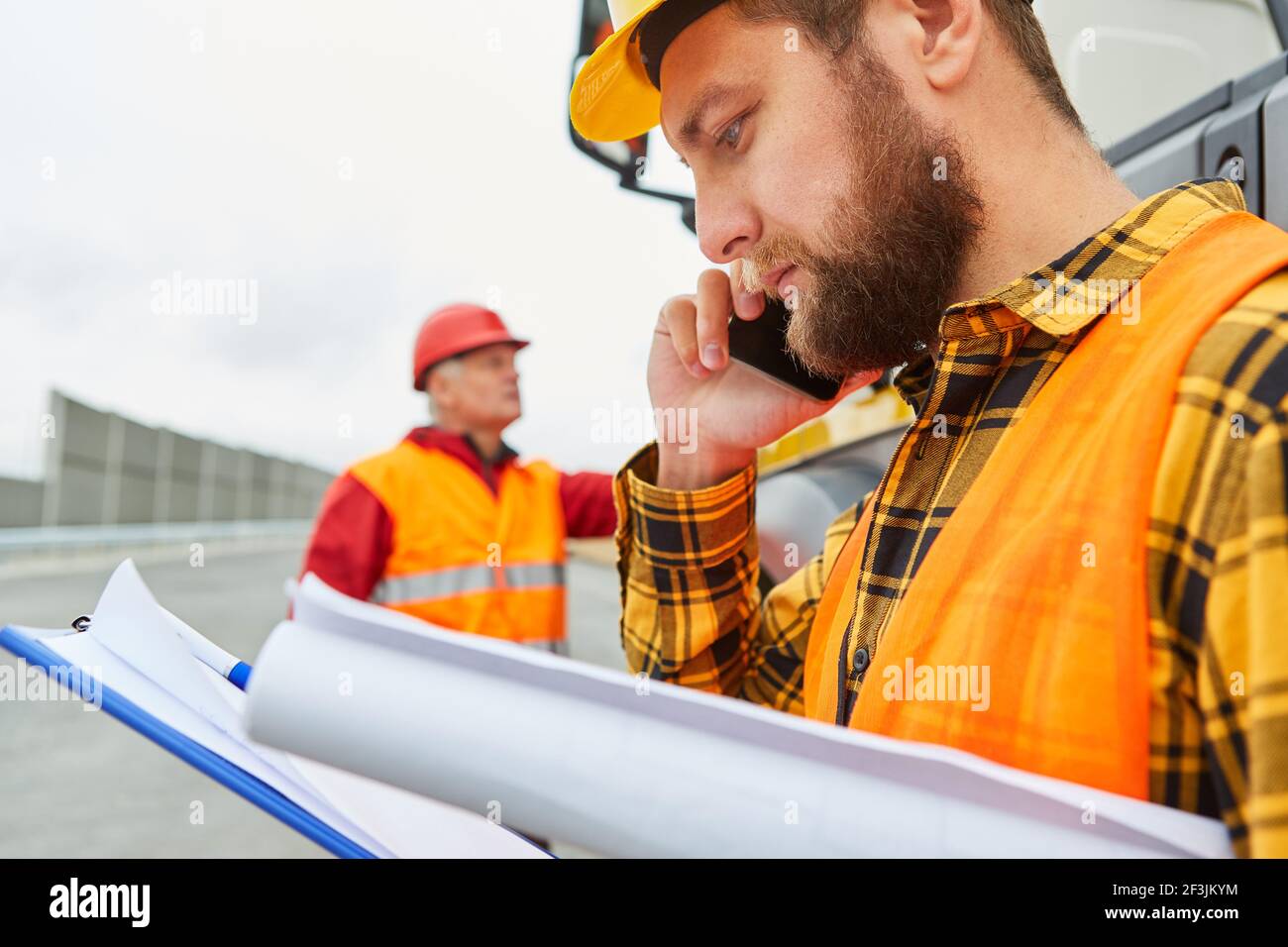 Travailleur de la construction avec des documents sur le téléphone avec téléphone portable sur le chantier de construction de la route Banque D'Images