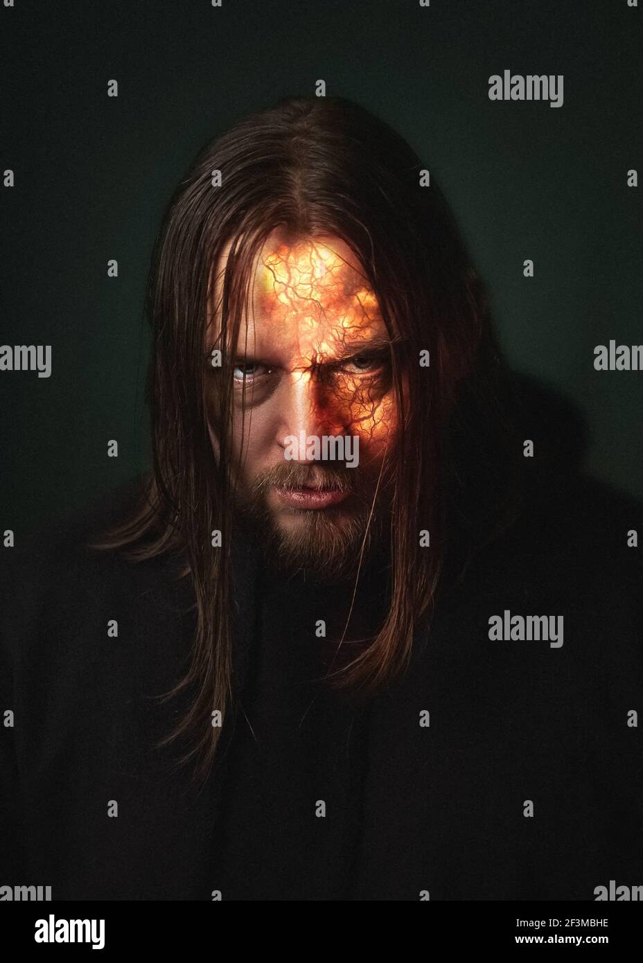Un homme démon avec un visage brûlant dans un feu Étincelles et fumée sur fond vert foncé Halloween diable horreur Banque D'Images