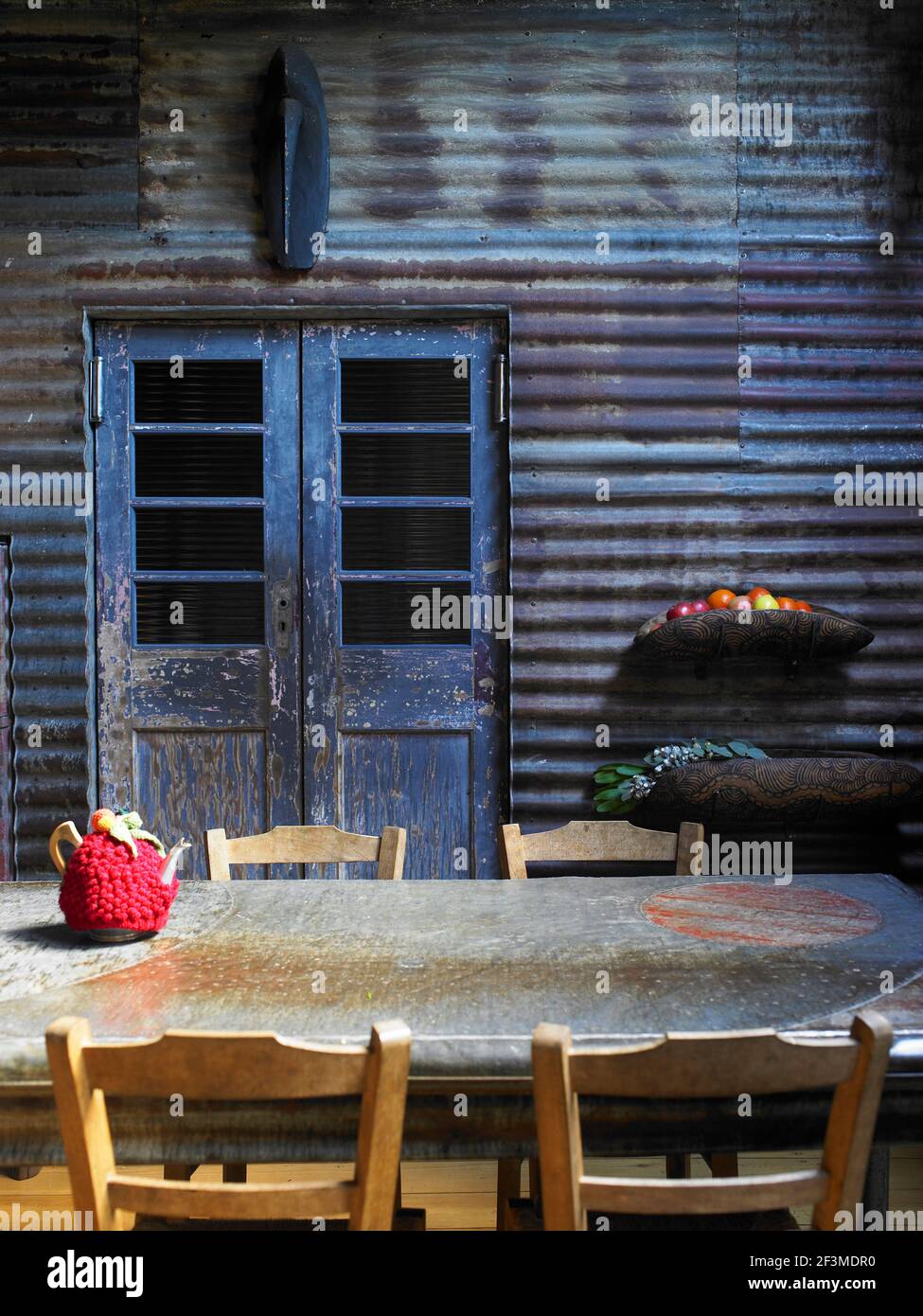 Mur ondulé avec porte peinte en vieilli et table rustique, thé à la framboise et bols à fruits muraux dans maison résidentielle, Australie. Banque D'Images