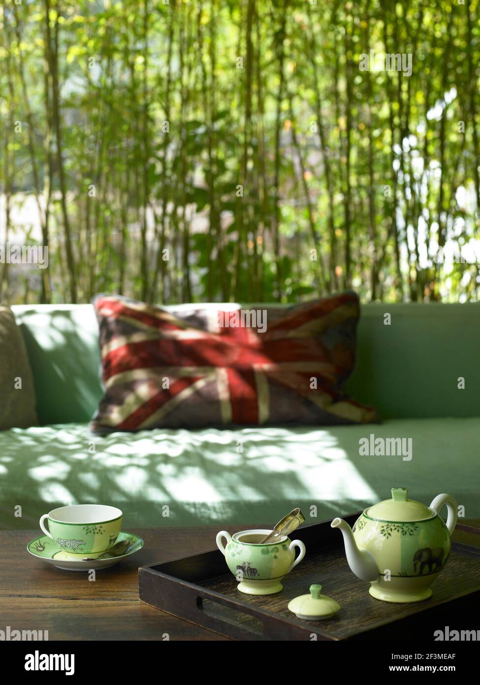 La lumière du soleil s'applique à l'extérieur, avec une théière en porcelaine sur une table en bois, un coussin Union Jack et un fond en bambou dans une maison résidentielle, aux États-Unis. Banque D'Images