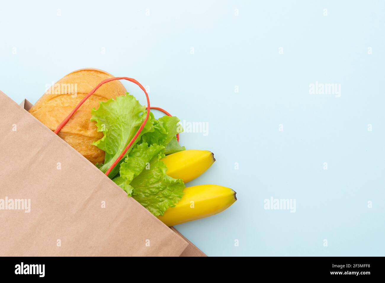 Sac de papier avec nourriture : feuilles vertes de salade, pain et banane. Disposer sur fond bleu, vue de dessus Banque D'Images
