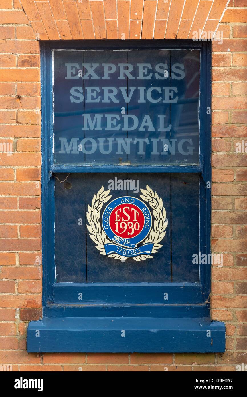 Glover & Riding, magasins militaires et civils de tailleurs à Aldershot, Hampshire, Angleterre, Royaume-Uni. Publicité de montage de la médaille de service express dans la fenêtre. Banque D'Images