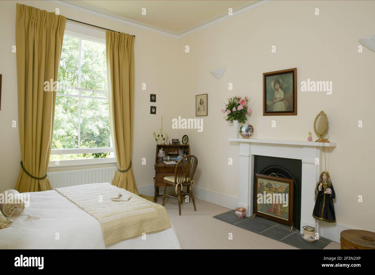 Chambre traditionnelle avec lit double, couvre-lit blanc, rideaux dorés, bureau et cheminée. Banque D'Images