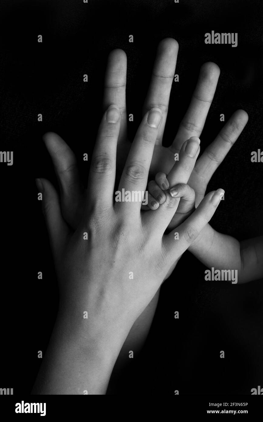 Nouveau-né tenant les mains du père et de la mère sur fond noir, photo en noir et blanc Banque D'Images