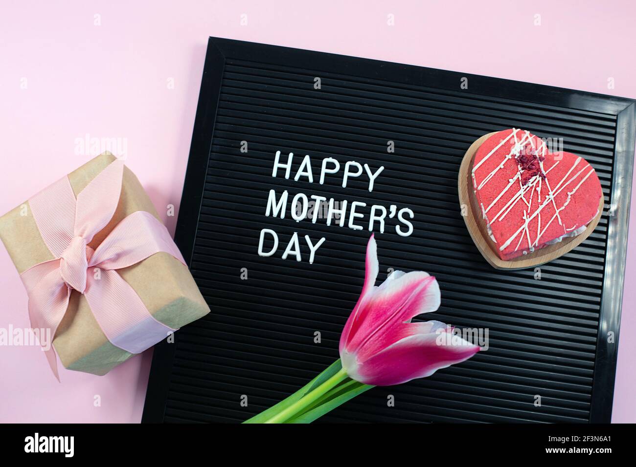 Lettrage noir avec lettres en plastique blanc avec citation Happy Mothers day et savon de fleur, coeur sur fond rose. Banque D'Images