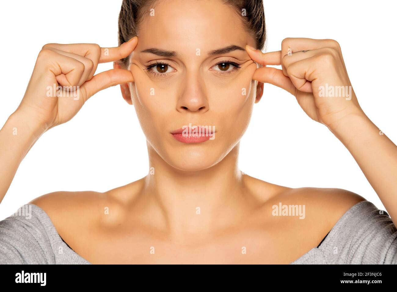 Jeune femme triste pinçant ses rides oculaires sur fond blanc Banque D'Images