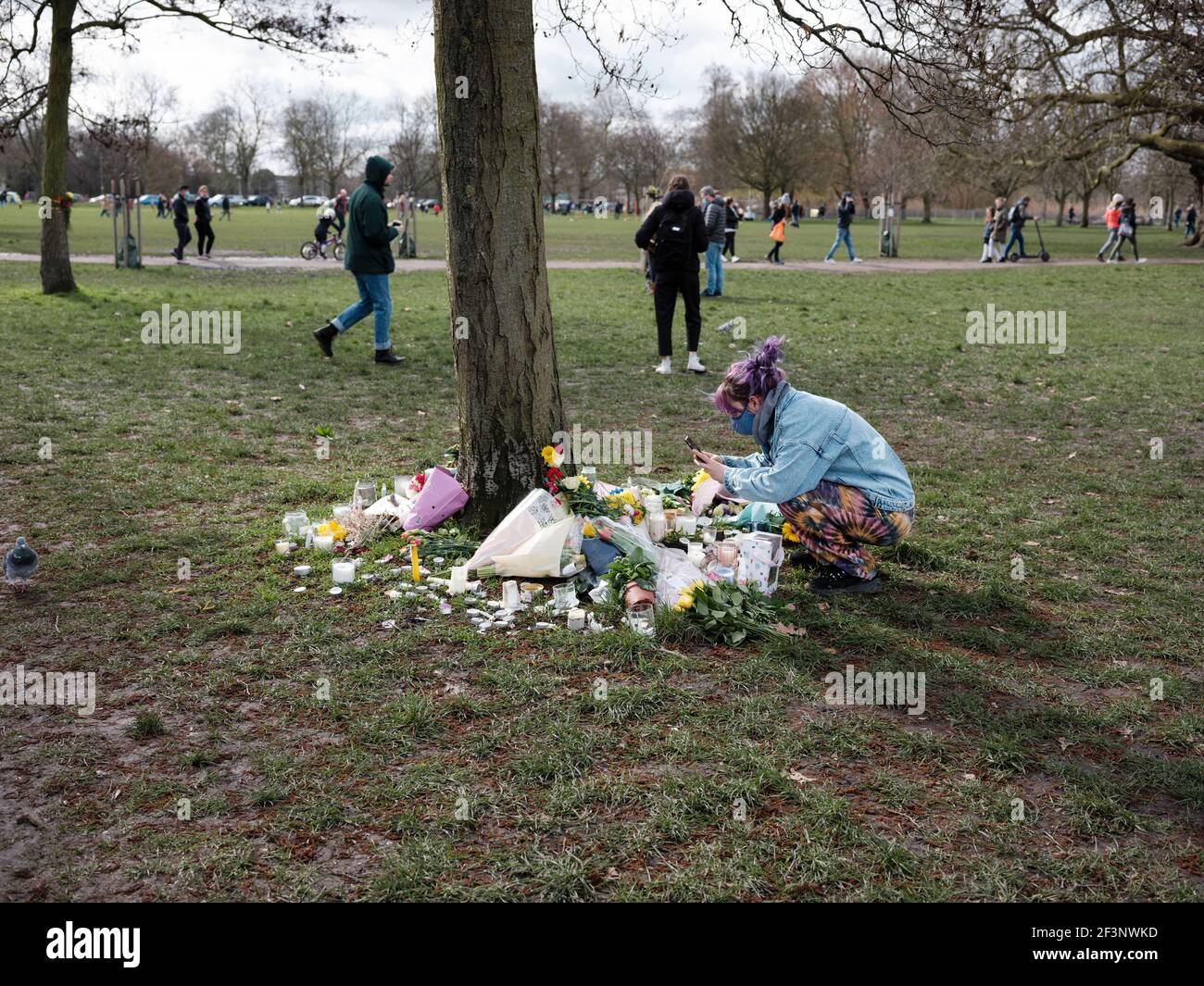 Un pleureur place des fleurs et des bougies pour Sarah Everard à la base d'un arbre, près du kiosque à Clapham Common, le 14 mars 2021 Banque D'Images