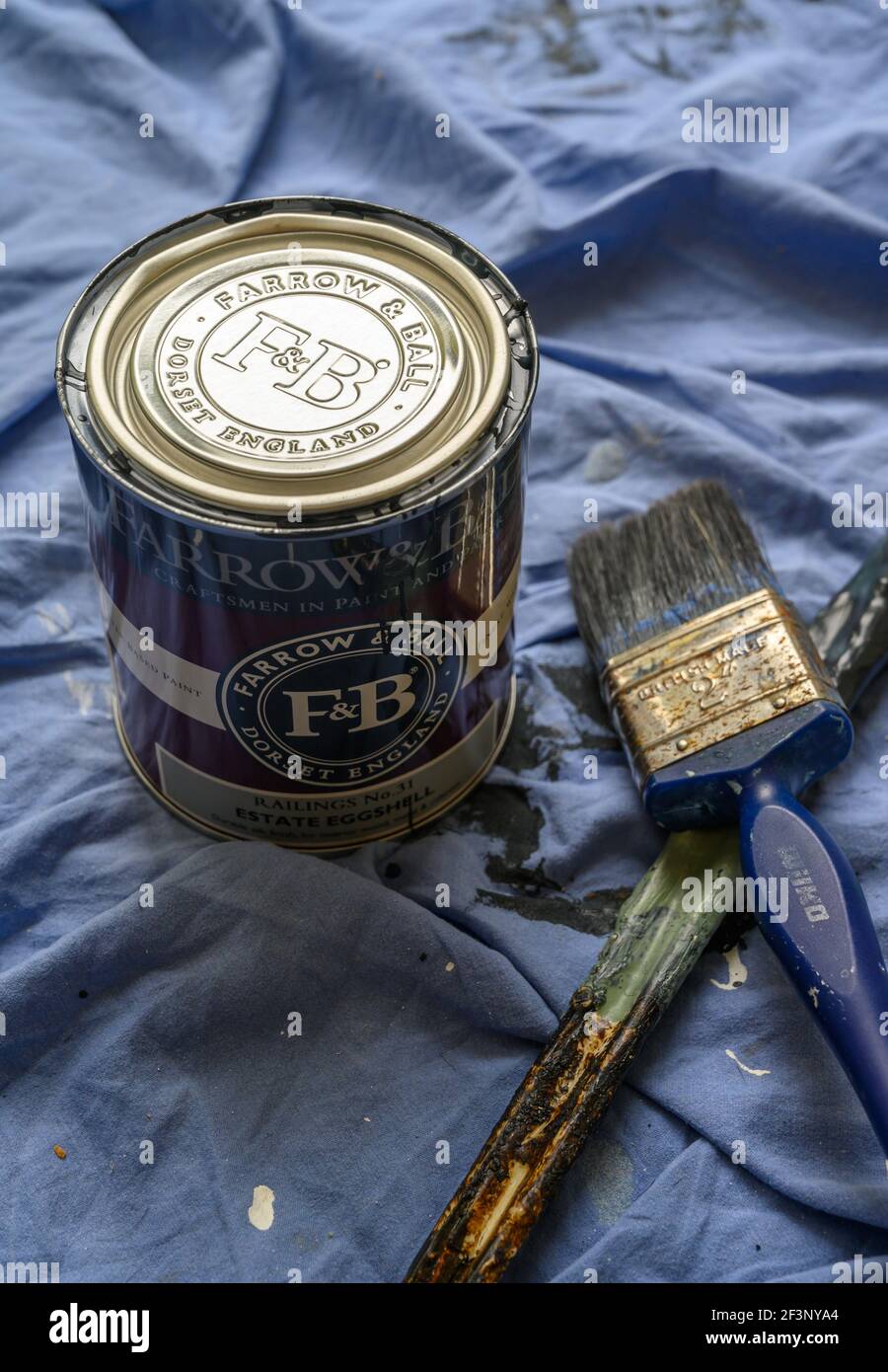 Une boîte de peinture Farrow & ball, n° de rambardes 31, fini coquille d'œuf Estate pour bois et métal d'intérieur avec brosse et bâton d'agitation sur la feuille de poussière bleue. Banque D'Images