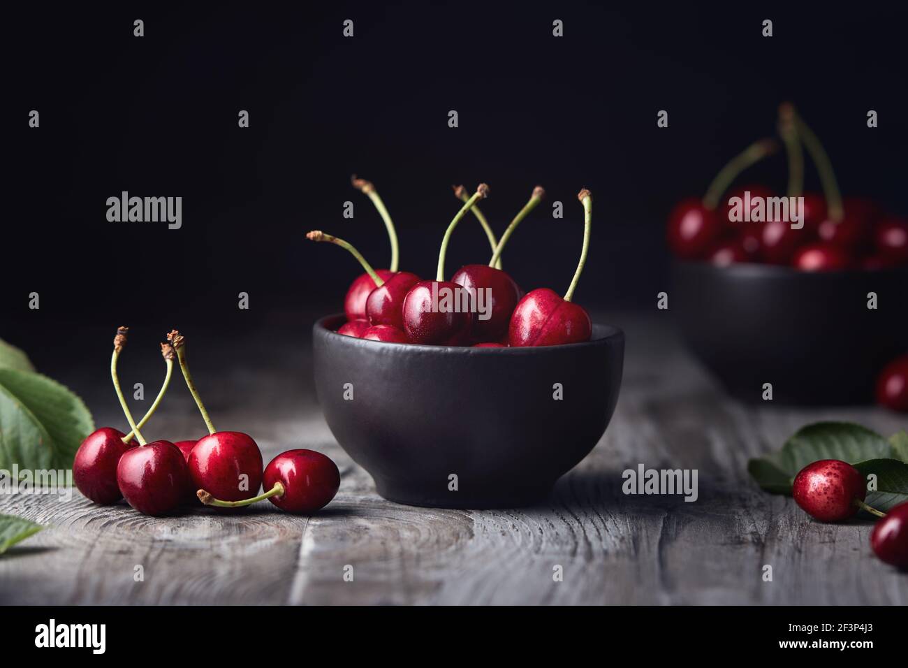 Cerises rouges mûres dans un bol et à côté sur une table en bois. Banque D'Images