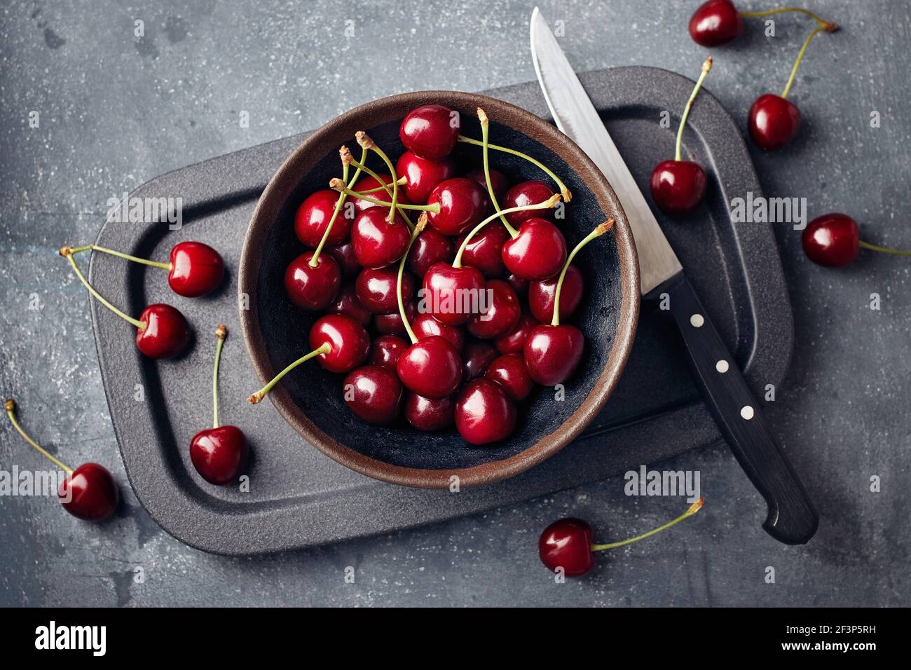 Cerises dans un petit bol et dispersées autour de la table. Banque D'Images