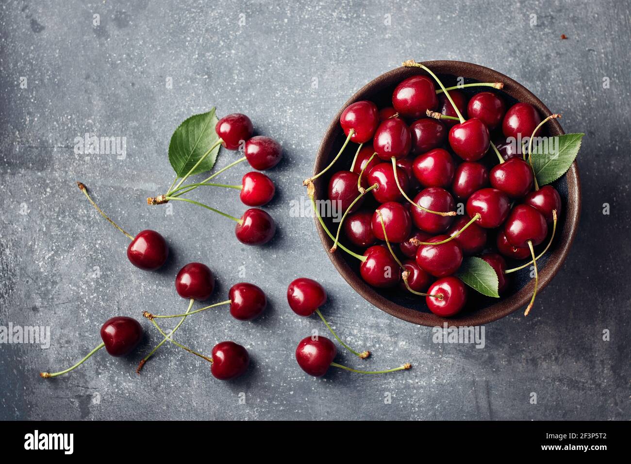 Cerises dans un petit bol et dispersées autour de la table. Banque D'Images