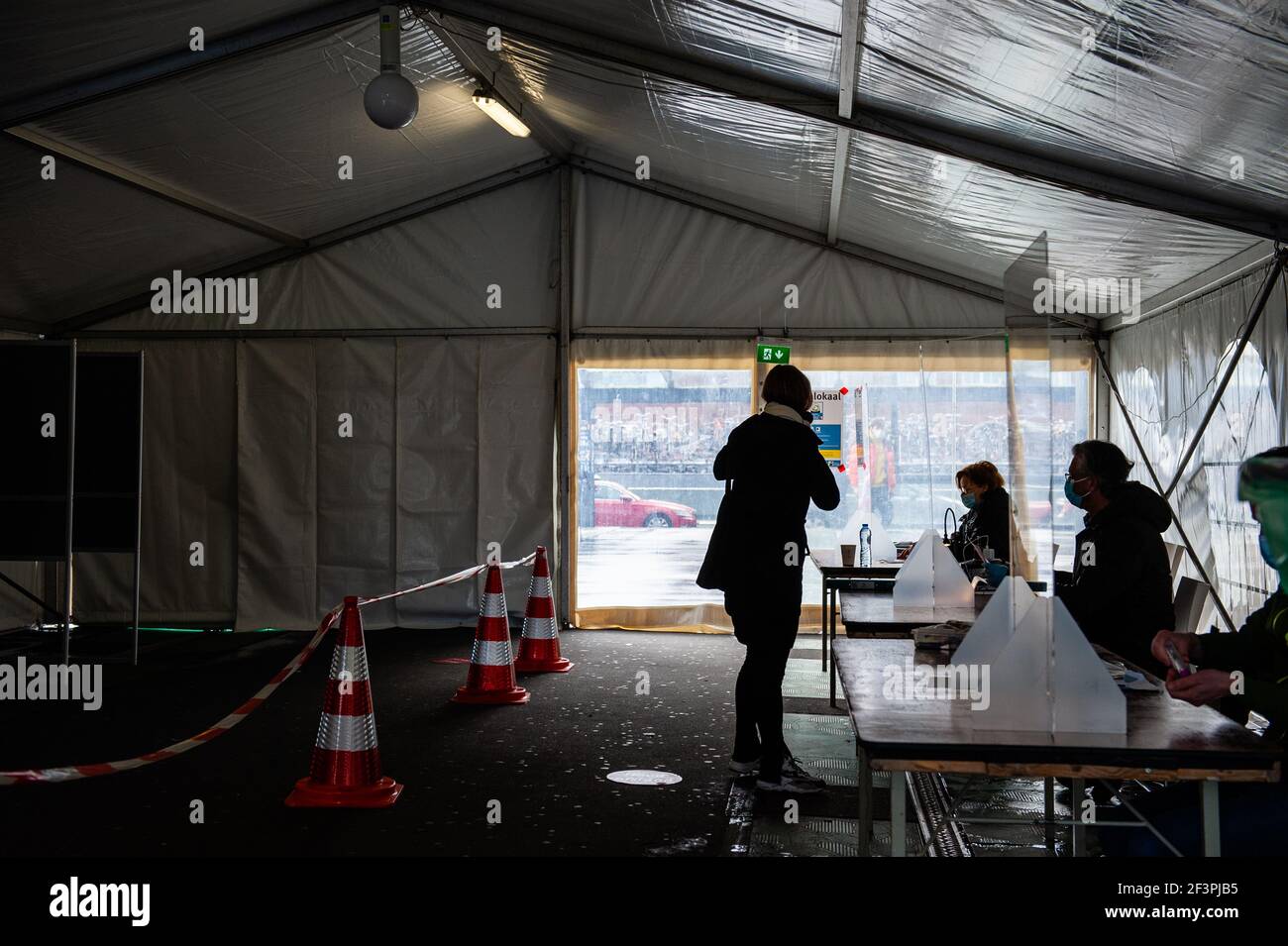 Une femme présentant son identification avant de la jeter vote.Netherlands est l'un des pays à tenir des élections générales en 2021 dans le cadre du confinement du coronavirus. Pour réduire le risque de contamination, le gouvernement a pris des mesures de protection contre les corona, telles que l'ouverture de bureaux de vote dans différents endroits comme des églises, des gares, des salles de concert, ainsi que l'installation de systèmes univoies et d'écrans en plastique. L'un des problèmes les plus épineux s'est avéré être le crayon rouge emblématique que chaque électeur hollandais utilise pour marquer son choix. Banque D'Images