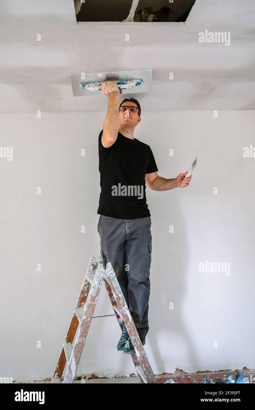 Plâtrier lissant le plafond en plâtre avec la truelle Banque D'Images