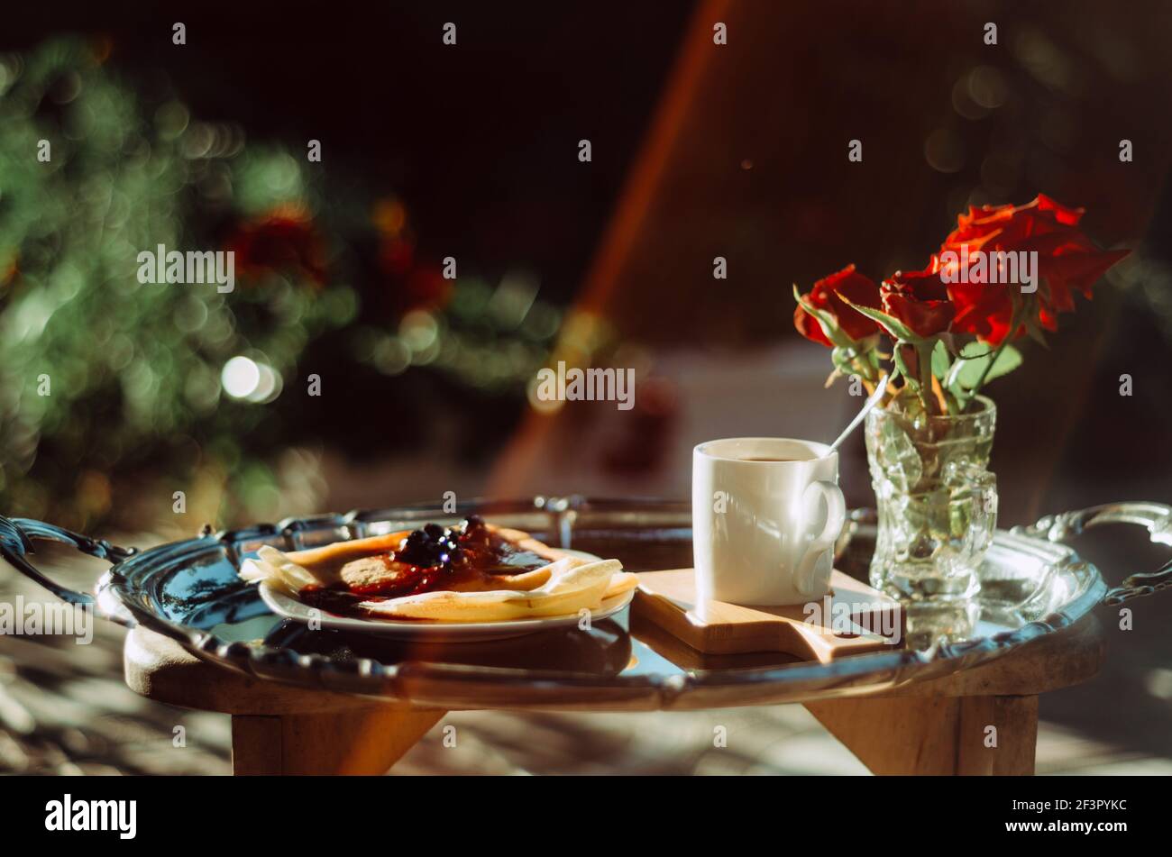 Brunch en plein air avec gros plan d'une tasse de café expresso, crêpes avec confiture et roses dans un verre, sur un plateau argenté vintage, avec lentille de lumière Banque D'Images
