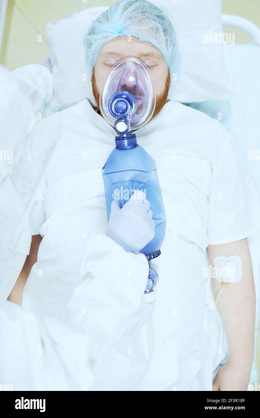 Vue en grand angle d'un patient mâle allongé sur un masque à oxygène sur le lit pendant le fonctionnement en salle d'opération Banque D'Images