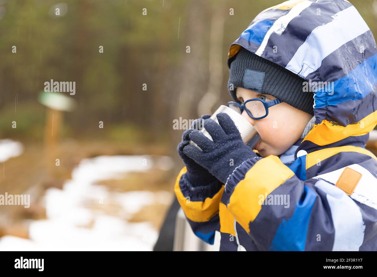 Un jeune garçon boit une boisson chaude d'une tasse par jour de raini froid. Repos, faire une pause pendant la randonnée. Concept de vie saine. Banque D'Images