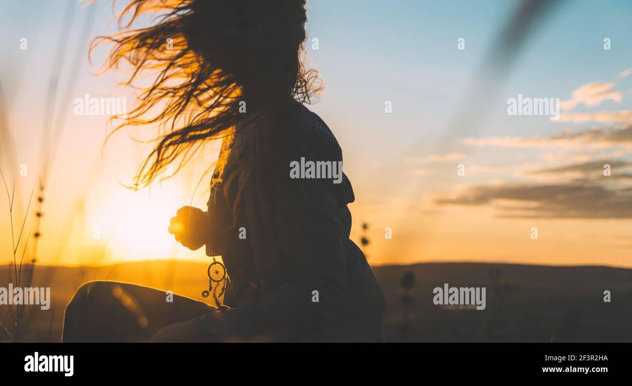 Silhouette d'une jeune femme avec ses cheveux en mouvement rétroéclairé par un magnifique coucher de soleil doré Banque D'Images