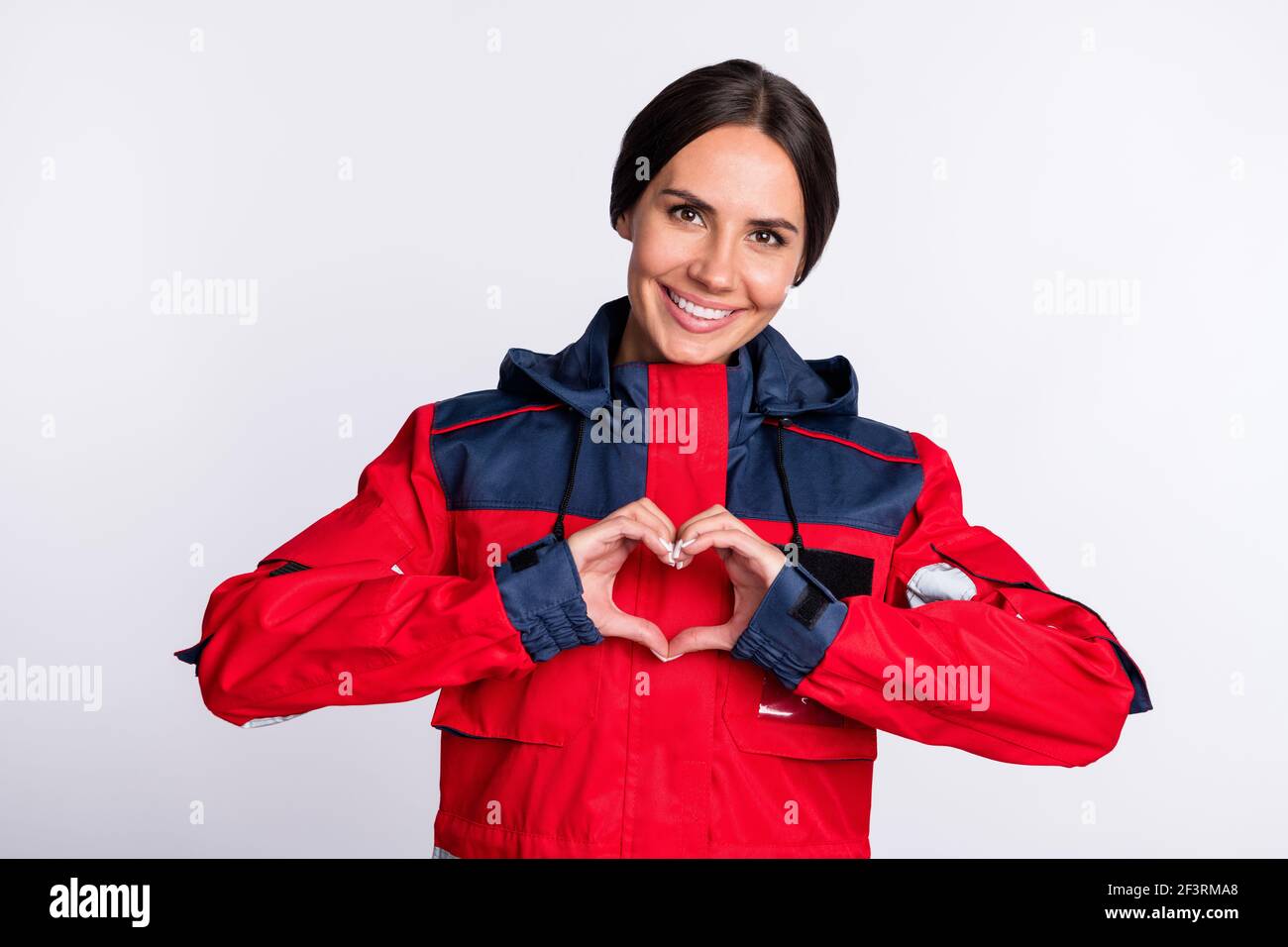 Photo de bonne humeur jeune femme ambulancier habillé rouge uniforme sourire montrant les doigts coeur isolé couleur blanc arrière-plan Banque D'Images