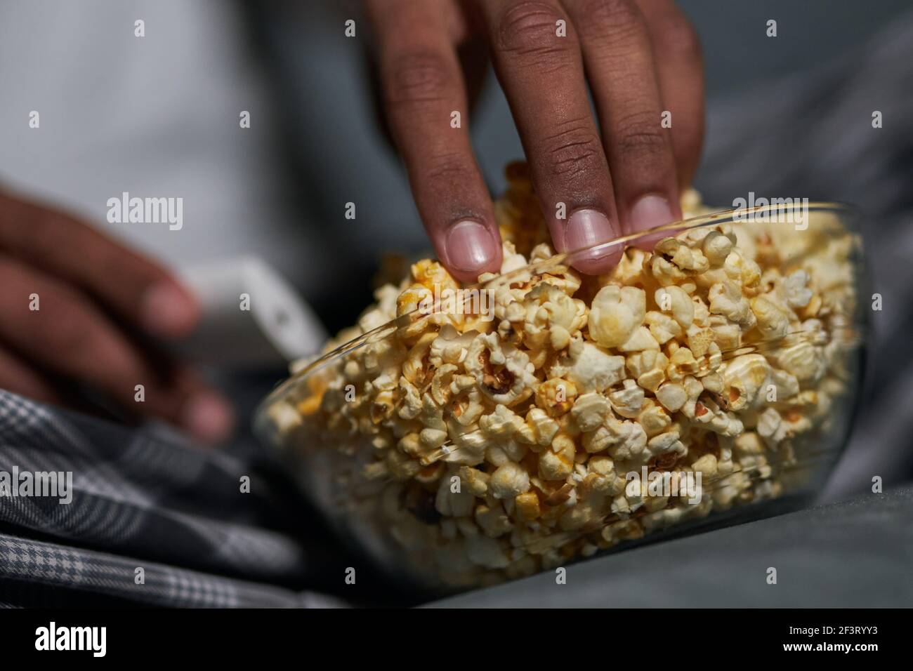 Bon goût. Gros plan sur une main masculine prenant du pop-corn dans un bol Banque D'Images