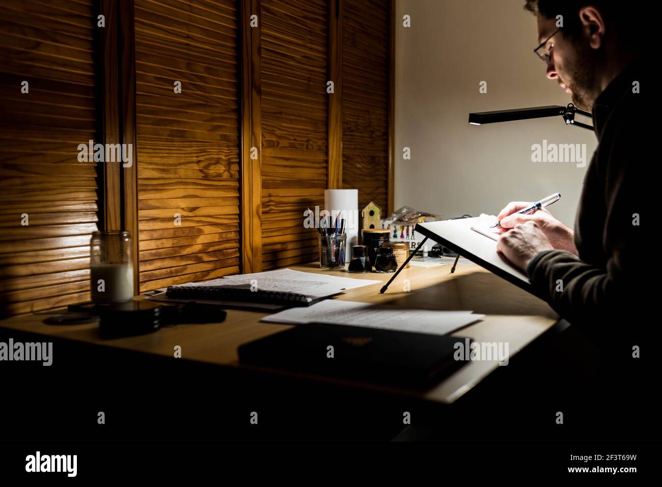 un homme assis à un bureau qui travaille tard la nuit à la maison. écrire avec un stylo et du papier. Banque D'Images