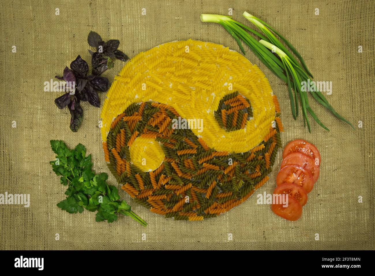 Le concept de yin yang. Signe yin yang sur le fond de burlap. On a utilisé des pâtes colorées aux colorants naturels, des oignons verts, des tomates et du persil. Banque D'Images