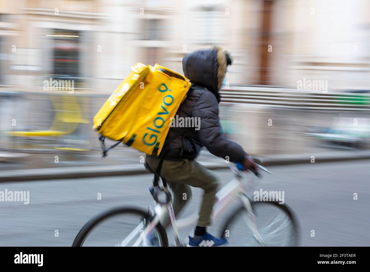 Photo floue avec mouvement du pilote de livraison de nourriture sur le vélo Avec Glovo box thermique jaune dans le temps de Covid Banque D'Images