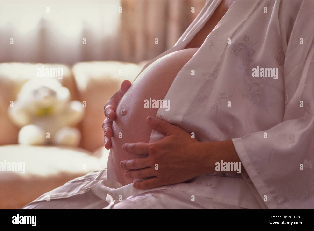 Femme enceinte en robe de soie tenant le ventre Banque D'Images