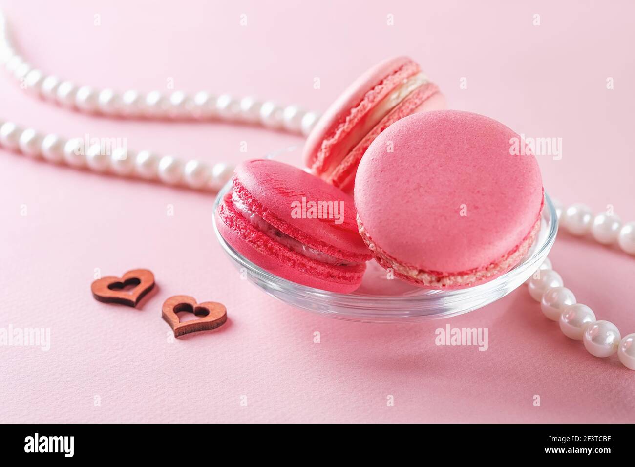 Peu de macarons roses et de perles blanches sur fond rose pastel. Romance, amour, concept de carte de vœux de Saint-Valentin. Dessert aux amandes françaises. Banque D'Images