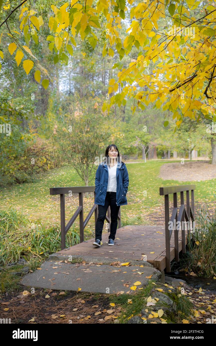 Une femme coréenne traverse une petite passerelle en automne à l'arboretum Finch de Spokane, Washington, États-Unis. Banque D'Images