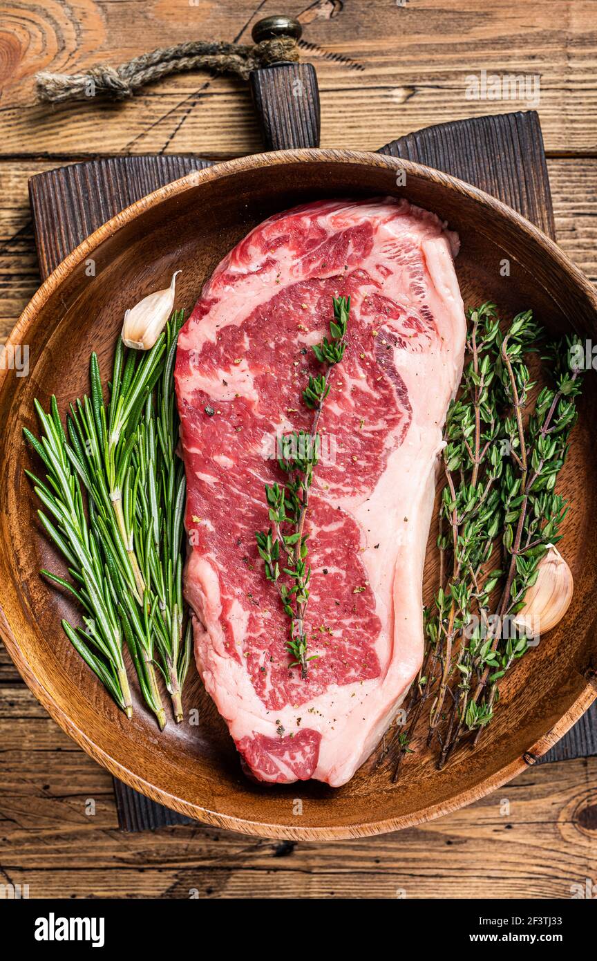 Steak de viande de bœuf frais de New york ou striploin dans une assiette en bois avec des herbes. fond en bois. Vue de dessus Banque D'Images
