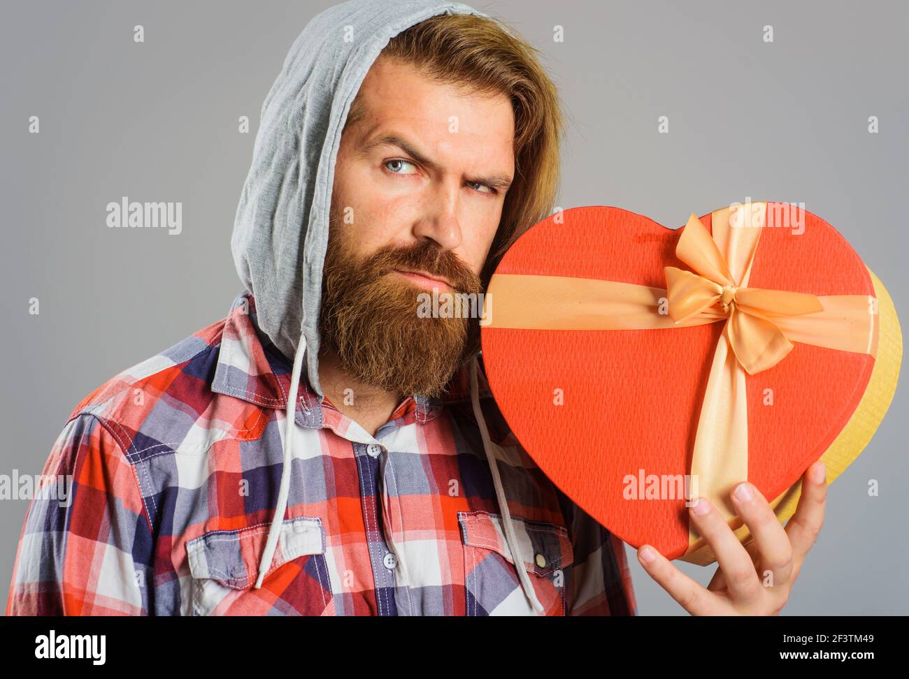 Un homme barbu tient une boîte cadeau en forme de coeur. Cadeau avec amour. Cadeau et cadeaux acheter. L'heure des cadeaux. Banque D'Images