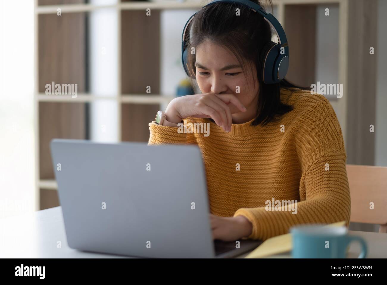 Portrait d'une femme asiatique étudiant en ligne avec un ordinateur portable tout en étant assise à la table et à l'ordinateur portable à la maison. Banque D'Images