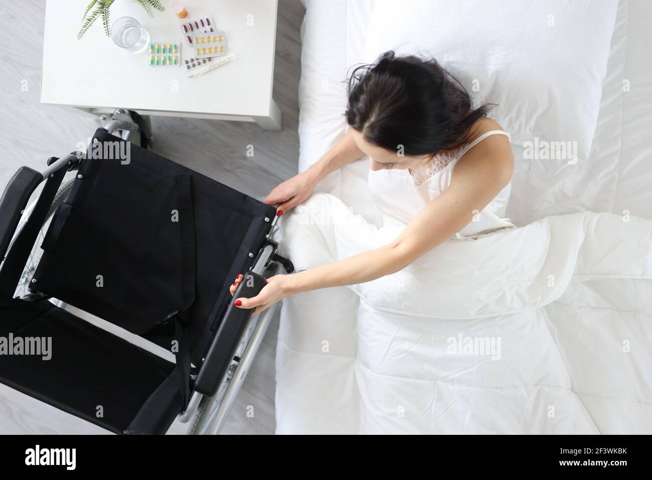 Une femme handicapée sort du lit et se tient sur un fauteuil roulant Banque D'Images