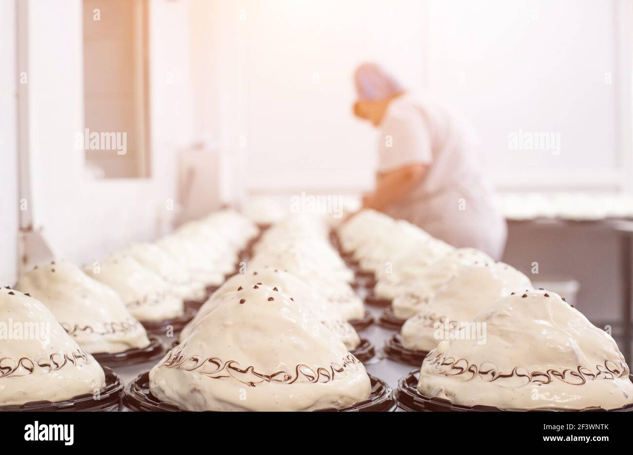Fabrication de gâteaux éponge avec crème dans une usine de confiserie. Cuisinier décore le gâteau avec la crème, le dessert sucré Banque D'Images