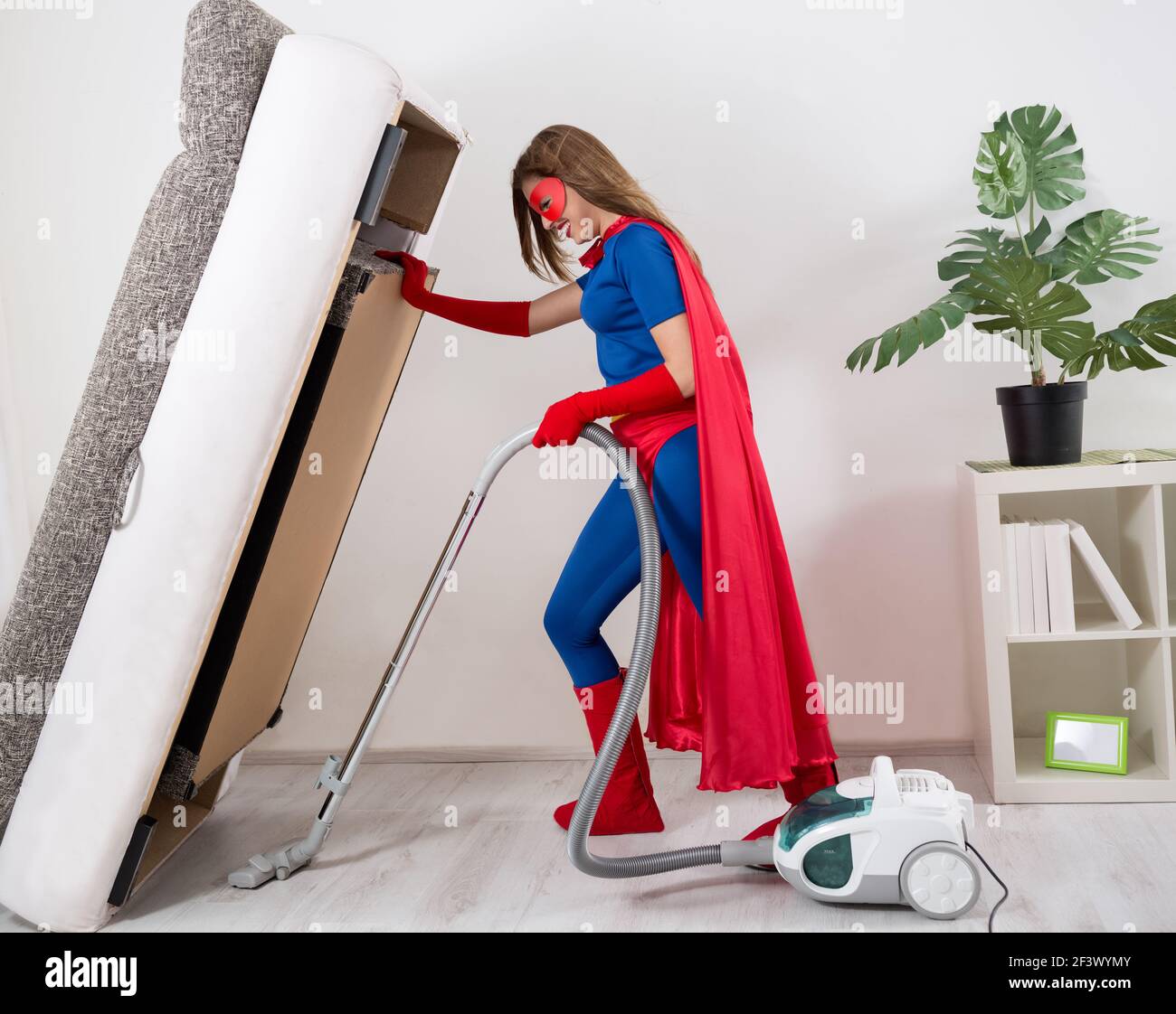 Belle femme super-héros passant l'aspirateur sous le lit Photo Stock - Alamy
