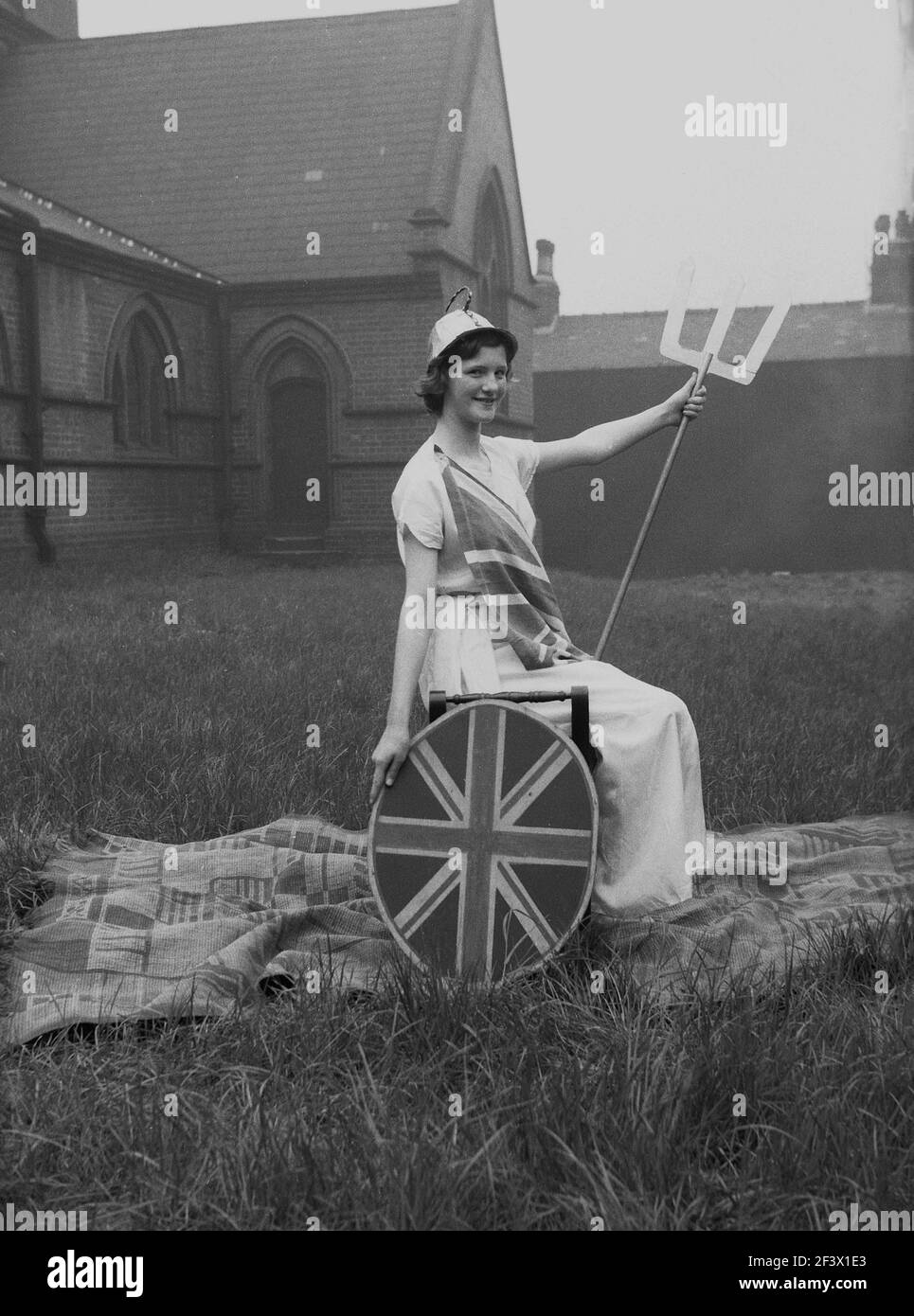 1958, historique, printemps et une adolescente dans son costume de parade, lance assise et bouclier d'Union Jack, posant dans le domaine d'une église pour sa photo, avant de prendre part au traditionnel festival du jour de mai, Leeds, Angleterre, Royaume-Uni. Banque D'Images