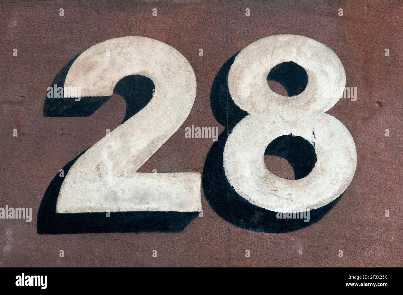 Gros plan du numéro vingt-huit peint à la main en peinture blanche avec UNE ombre portée noire sur UN mur en terre cuite à Londres, Royaume-Uni Banque D'Images