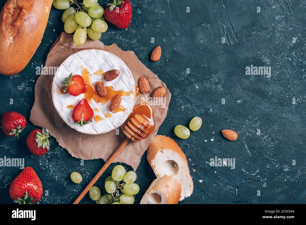 Camembert français servi sur du raisin, du miel, de l'amande, des fraises, de la baguette sur fond sombre. Vue de dessus. Copier l'espace. Nuit romantique Banque D'Images