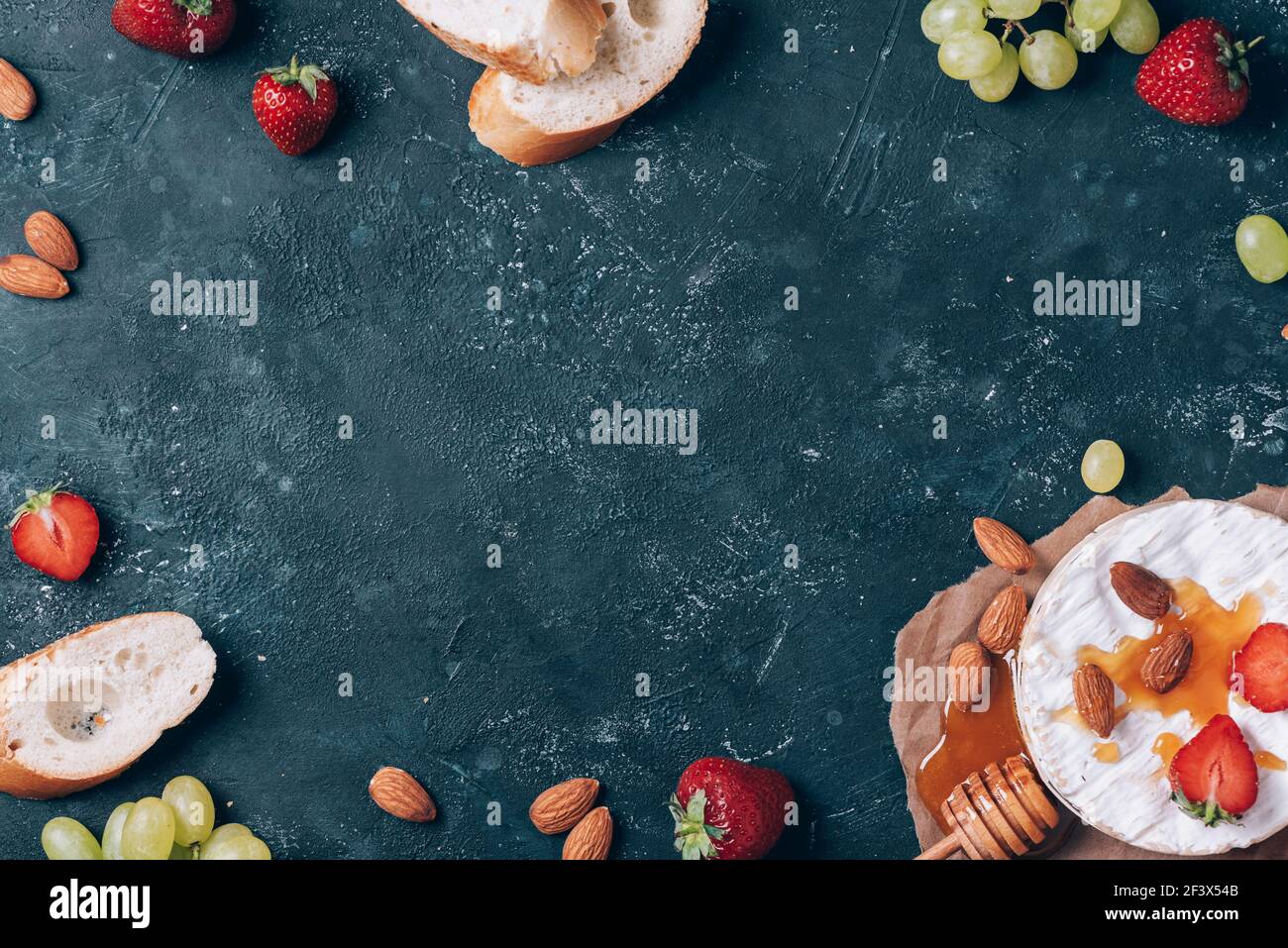Camembert français servi sur du raisin, du miel, de l'amande, des fraises, de la baguette sur fond sombre. Vue de dessus. Copier l'espace. Nuit romantique Banque D'Images